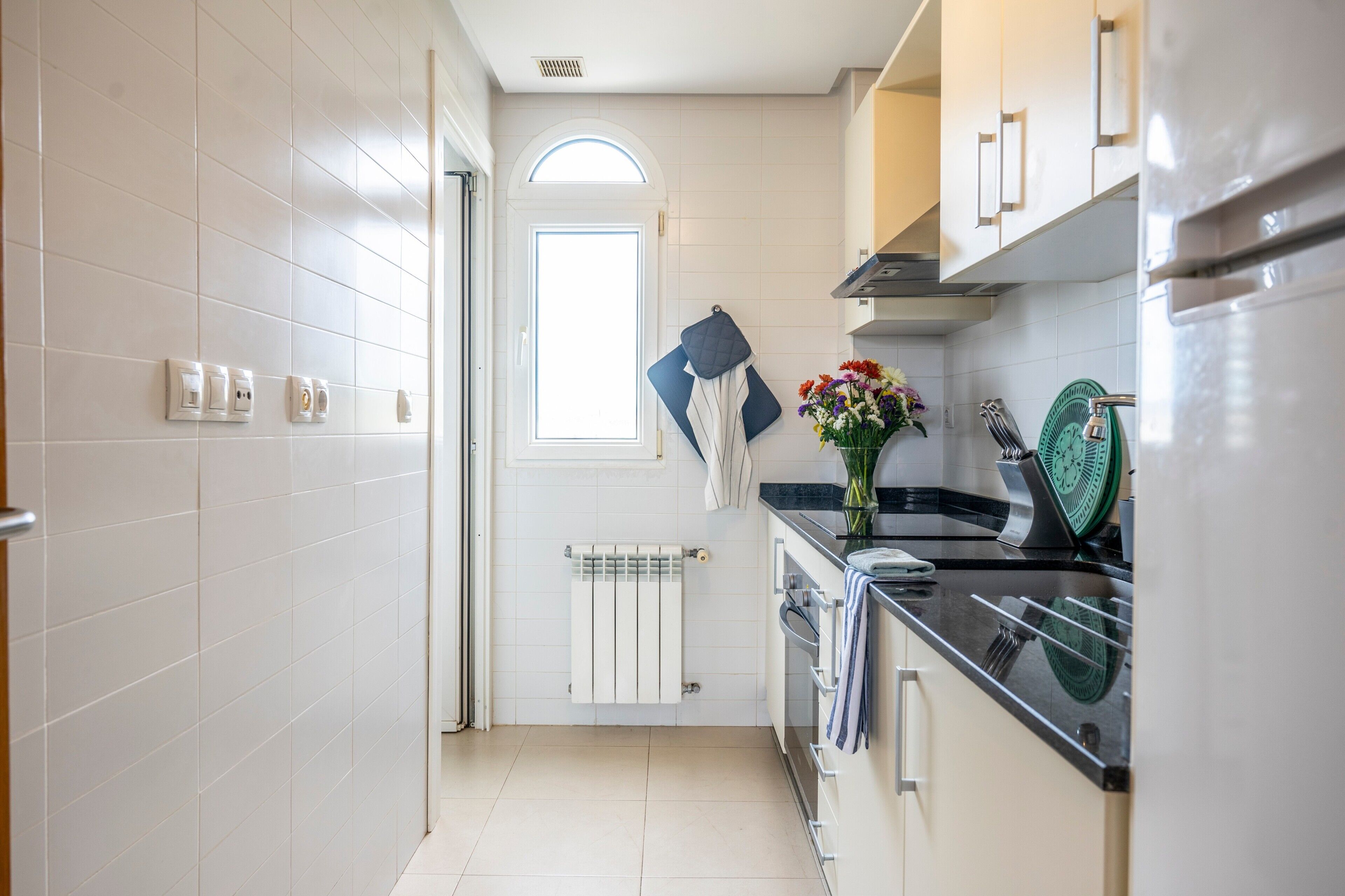 A kitchen with white tiles, a stove, a window, and a radiator.