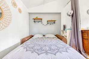 Una camera da letto con un letto, due mensole a parete con fiori, una ventola a soffitto e un comodino.