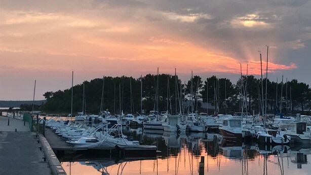 Un puerto deportivo con barcos amarrados, una superficie de agua tranquila y un cielo al atardecer.