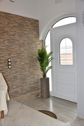 A hallway with a stone wall, a potted plant, a white door with a window, and a tiled floor.
