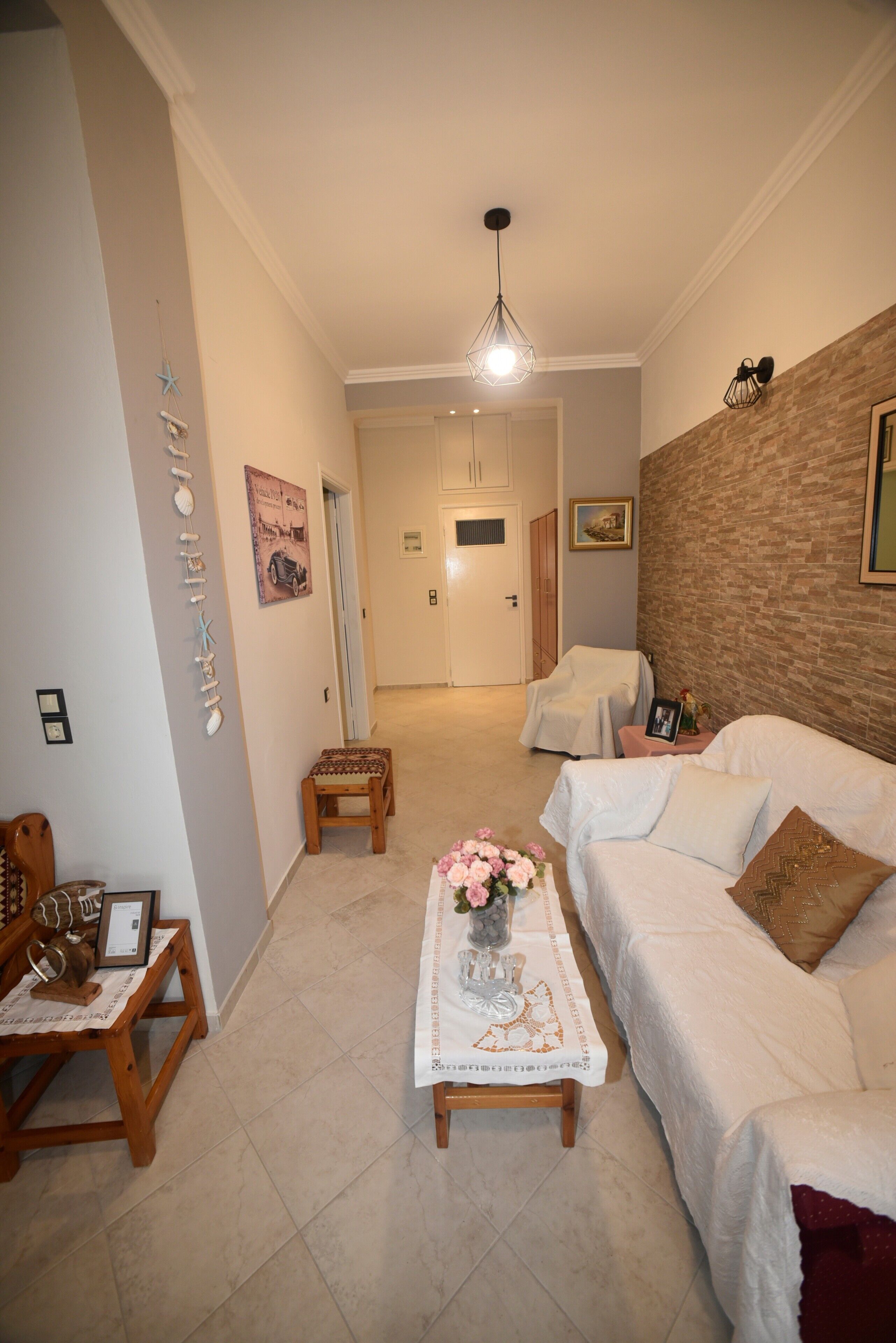 Sala de estar com sofá branco, mesa de centro com um vaso, um banco de madeira e parede de tijolos como destaque.