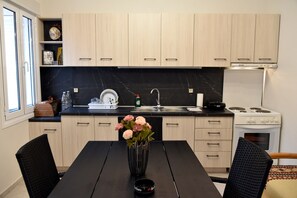 Une cuisine moderne avec des meubles de couleur bois clair, un plan de travail noir, un évier en acier inoxydable, une cuisinière et une table à manger avec des chaises.