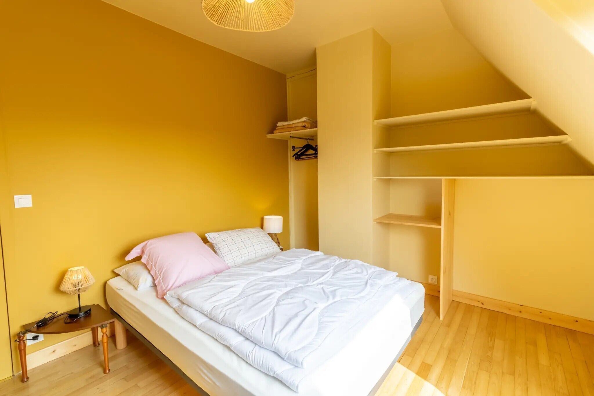 A bedroom with a bed, bedside table, lamp, and a closet with shelves.