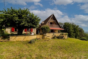Une maison en pierre avec un toit rouge, un balcon et un mur de pierre qui entoure la propriété.