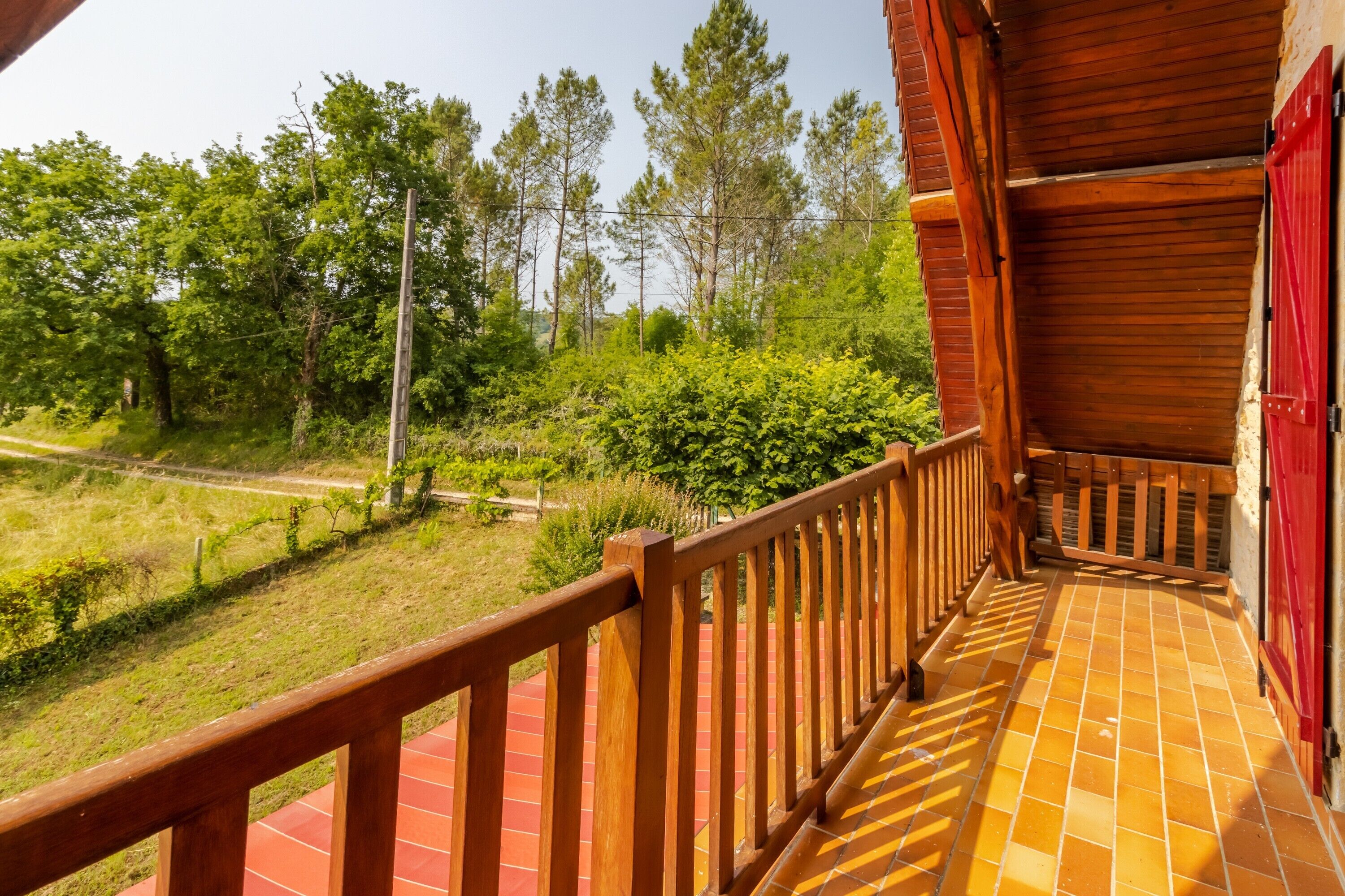 Ein Holzbalkon mit Fliesenboden, der auf eine Rasenfläche mit Bäumen und einer Straße blickt.