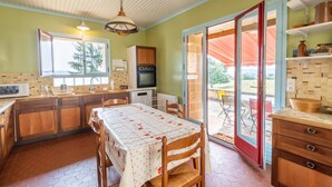 Una cocina con armarios de madera, una mesa de comedor con mantel floral, un microondas, un refrigerador y vistas al aire libre a través de una puerta de vidrio.