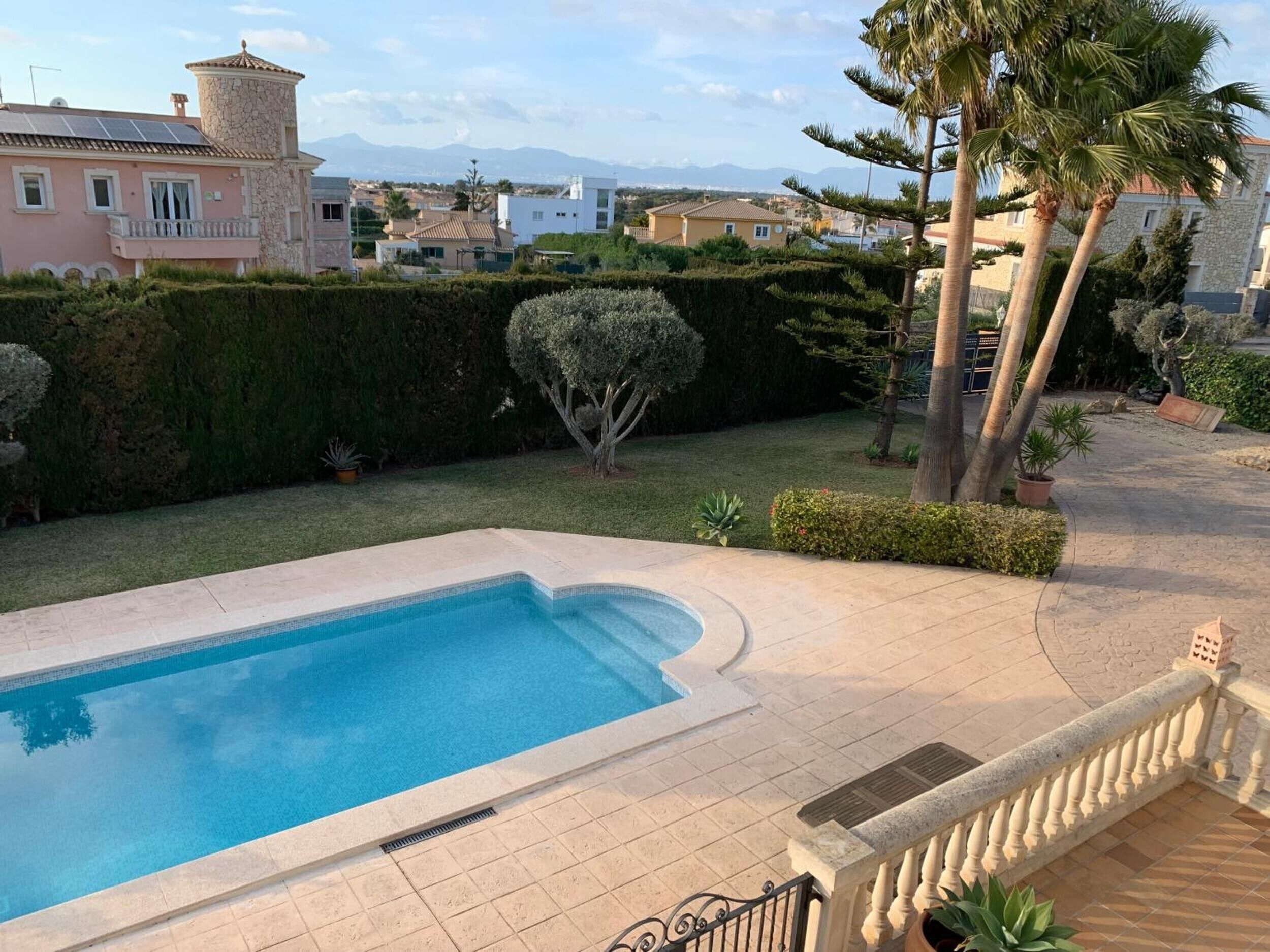 Une piscine à bord incurvé, entourée d’une terrasse dallée et d’une haie basse.