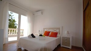 A hotel room with a bed, a nightstand, a lamp, and a view of a balcony. - Villa 'Cunill' with Sea View, Wi-Fi and Air Conditioning (Llucmajor)