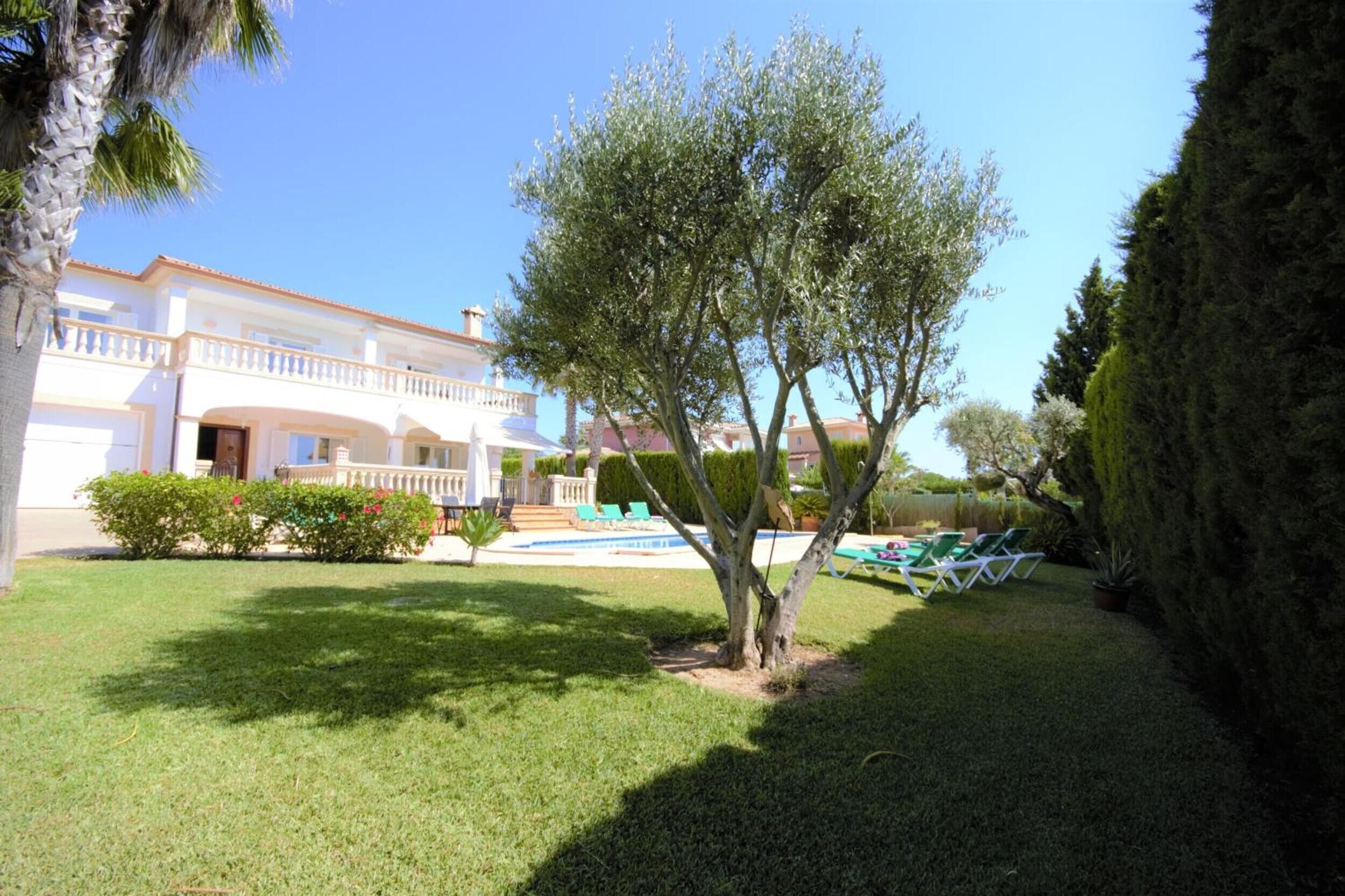 A white building with a balcony, a swimming pool, and green lawn furniture.