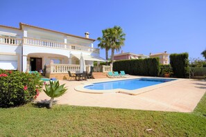 Una casa de dos pisos con piscina, un patio con sillones de descanso y un jardín bien cuidado.
