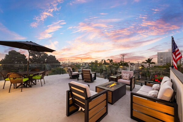 A rooftop patio with outdoor furniture, a fire pit, and an American flag.
