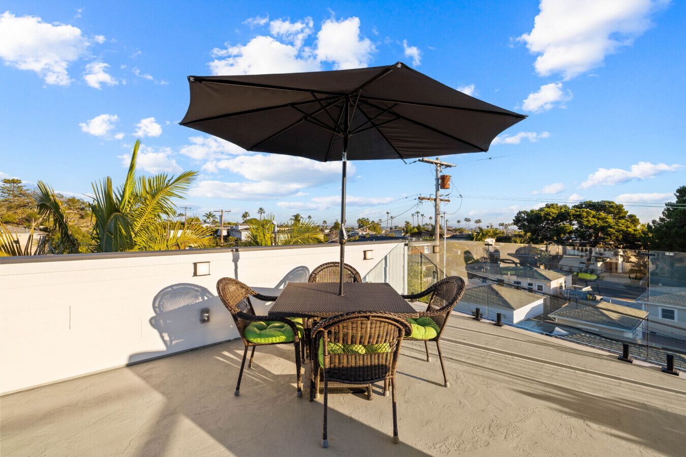 Une terrasse sur le toit, avec une table et des chaises, un parasol et une vue sur le quartier environnant.