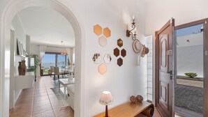 A hallway with a wooden bench, a wall-mounted lamp, hexagonal wall decor, and an open door leading outside.