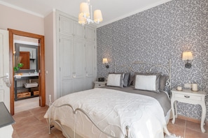 Een slaapkamer met een groot bed, een kledingkast, nachtkastjes en behangpapier met een patroon.