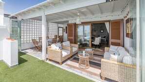 A covered outdoor seating area with wicker furniture, a glass door entrance, and a view into the interior.