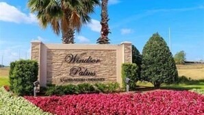 Une enseigne indiquant « Windsor Palms », avec une façade en pierre, entourée d’un aménagement paysager soigné et de palmiers.