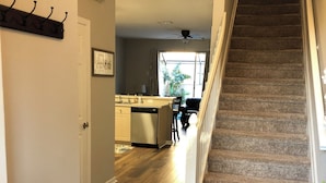 Un escalier menant à un deuxième étage, un coin cuisine avec une table à manger, et un banc au premier plan.