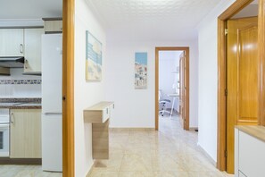 A kitchen with white cabinets, a countertop, and a refrigerator. There is a hallway leading to a dining area with a table and chairs.