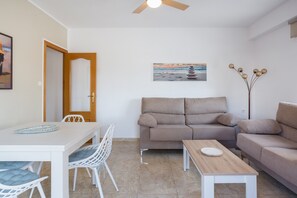 A living room with a sofa, a dining table with chairs, a coffee table, a ceiling fan, and a painting on the wall.
