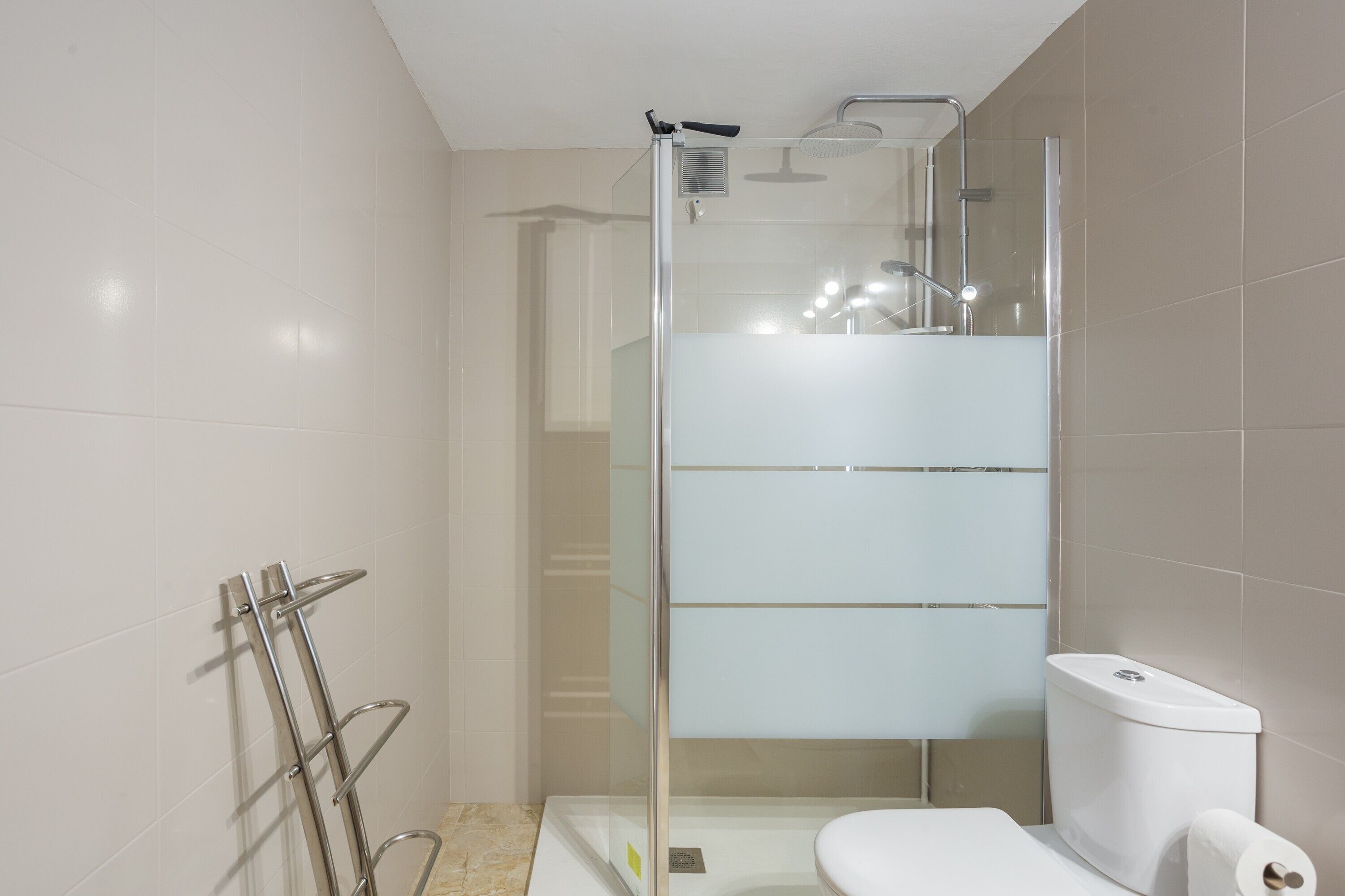 Une salle de bain moderne dotée d’une douche à parois de verre, de toilettes et d’un porte-serviettes.
