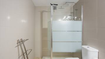 Une salle de bain moderne dotée d’une douche à parois de verre, de toilettes et d’un porte-serviettes.