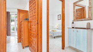 A hallway with wooden doors, a bed with a white bedspread, a bedside table, and a cabinet with a mirror.