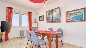 A dining area with a wooden table, blue chairs, a red umbrella, and artwork on the walls.