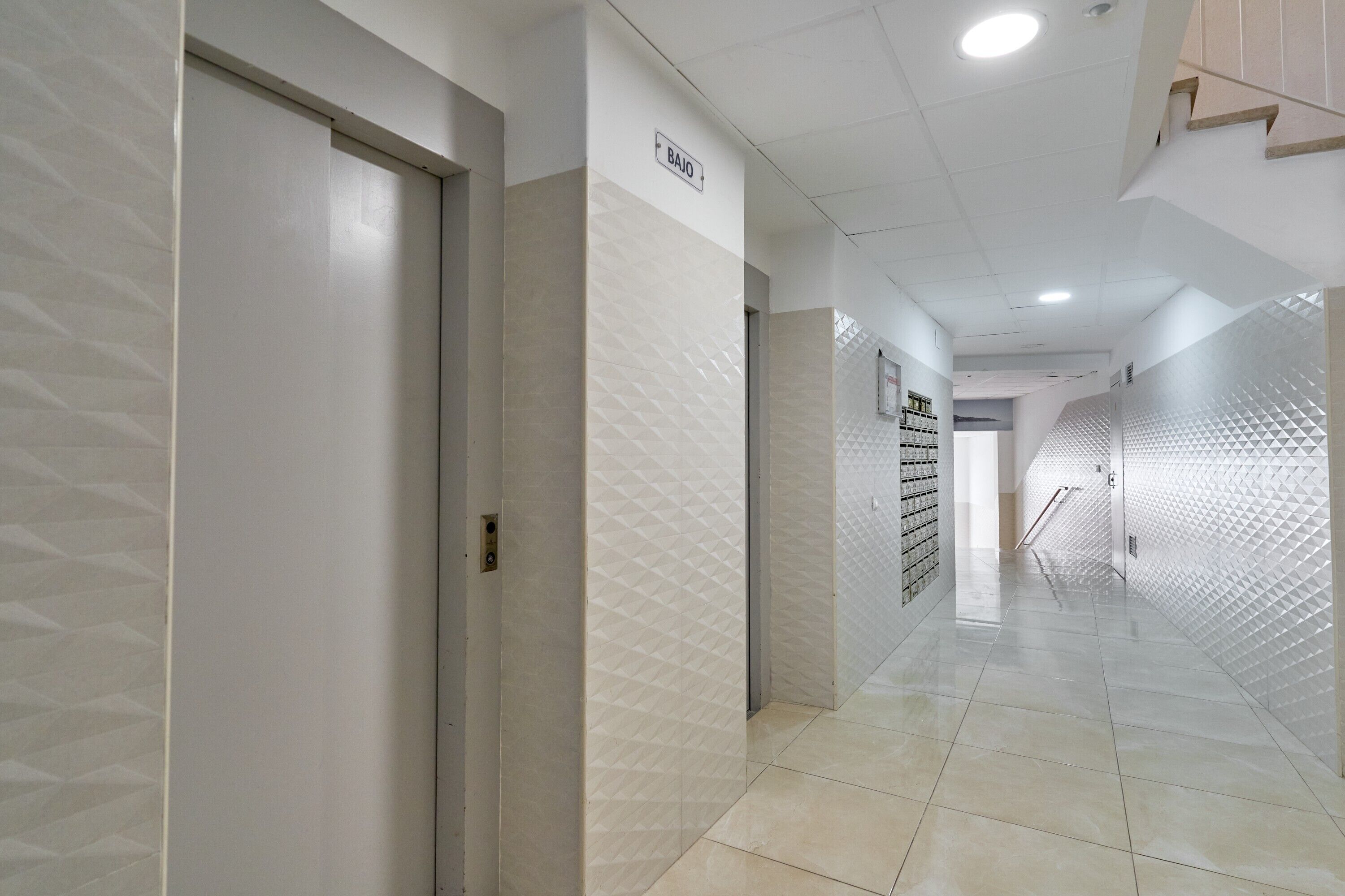 A hallway with a sign indicating the direction to the basement, tiled floors, and a wall with a geometric pattern.