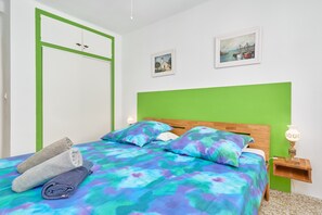 Un lit avec une tête de lit verte, deux oreillers, une serviette enroulée et une table de chevet avec une lampe.