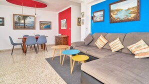 A living room with a sofa, a dining table with chairs, a red ceiling light, and framed artwork on the walls.