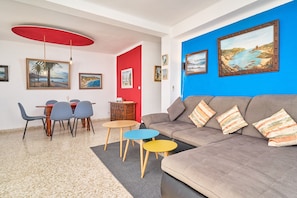 Un salon avec un canapé, une table à manger et des chaises, un luminaire rouge au plafond et des œuvres d’art encadrées accrochées aux murs.