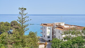 A coastal building with a tiled roof, surrounded by greenery and overlooking the sea.