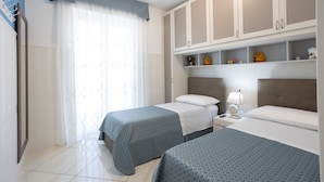 Une chambre d’hôtel avec deux lits, une armoire, une table de chevet et une fenêtre avec des rideaux légers.