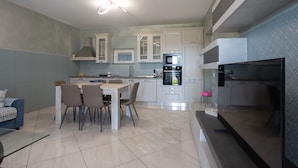 Une cuisine moderne avec des meubles blancs, un coin repas comprenant une table et des chaises, et un four encastré.