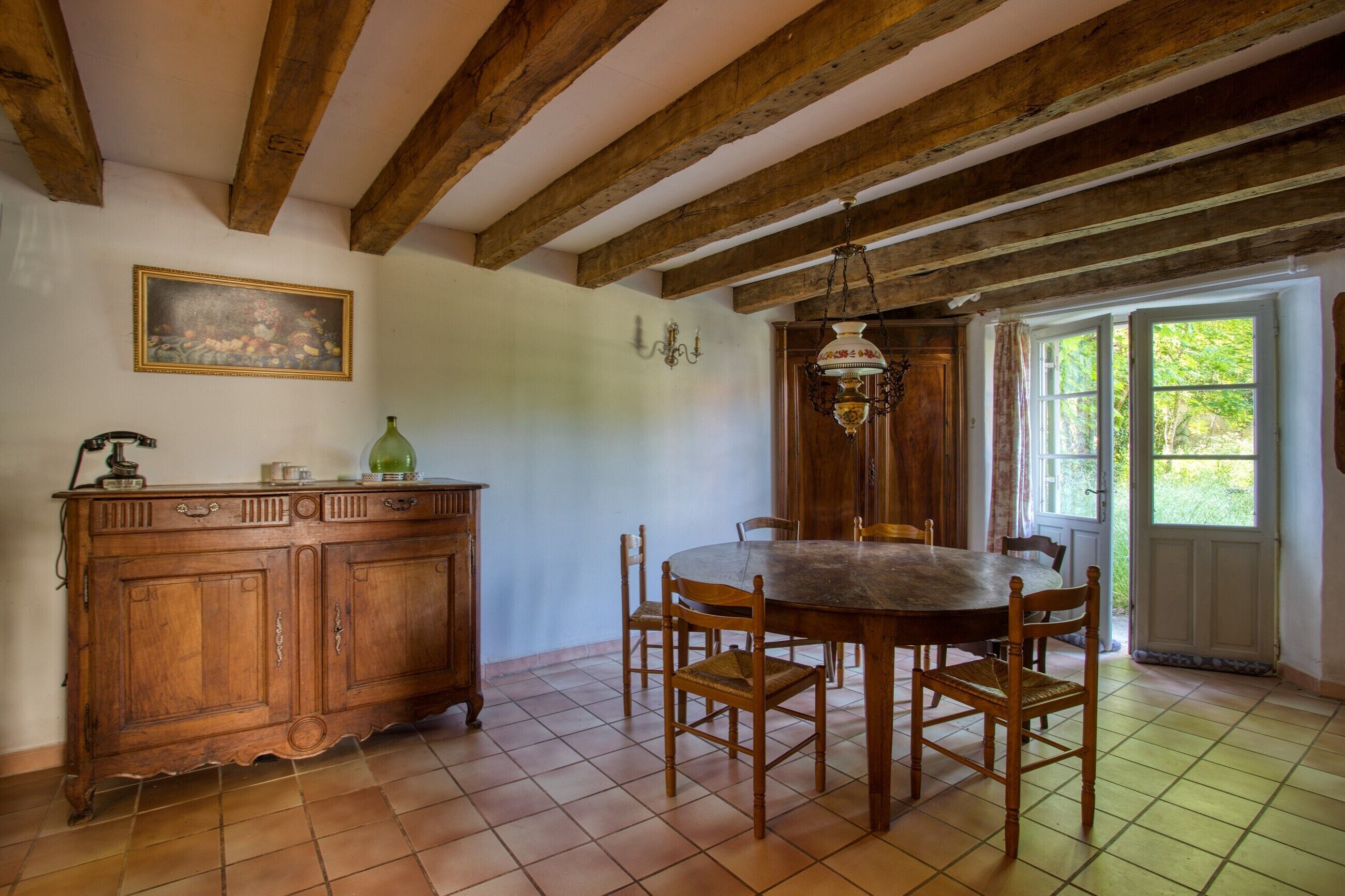Una sala da pranzo con un tavolo e sedie in legno, un armadietto, un quadro appeso al muro e una finestra con tende.