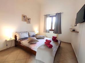 A bedroom with a bed, bedside lamps, a window with curtains, a flat-screen TV, and artwork on the wall.