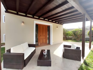 A covered outdoor seating area with a sofa, two armchairs, and a coffee table.