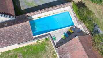 An aerial view of a rectangular swimming pool with a brick border, surrounded by a grassy area and a paved walkway.