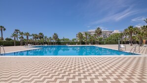 A swimming pool with a chevron-patterned deck, surrounded by palm trees and a clear blue sky. - Apartment 'Isla Canela' with Sea View, Wi-Fi and Air Conditioning (Ayamonte)
