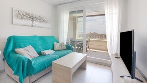 A modern living room with a sofa, a coffee table, a flat-screen TV, and a balcony with a city view. - Apartment 'Isla Canela' with Sea View, Wi-Fi and Air Conditioning (Ayamonte)