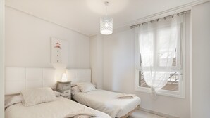 A bedroom with two beds, a bedside table with a lamp, a window with curtains, and a wall-mounted artwork. - Apartment 'Isla Canela' with Sea View, Wi-Fi and Air Conditioning (Ayamonte)