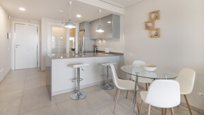 A modern kitchen with a central island, bar stools, a round glass table, and pendant lighting. - Apartment 'Isla Canela' with Sea View, Wi-Fi and Air Conditioning (Ayamonte)