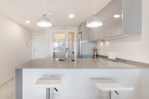 A modern kitchen with a central island, pendant lighting, and a view to the living area.