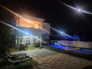 Ein Außenbereich bei Nacht mit Pool, Liegestühlen und einem Gebäude mit beleuchteten Fenstern.