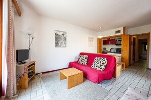 Una sala de estar con un sofá rojo, una mesa de centro de madera, un televisor y un estante pequeño de madera.
