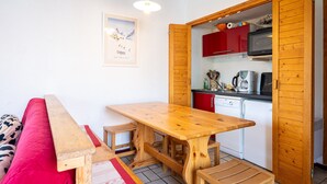 Ein gemütlicher Wohnraum mit Holztisch, einem roten Sofa und einer Küchenzeile mit roten Schränken und einer Mikrowelle.