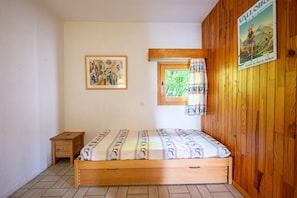 Un dormitorio pequeño con una cama de madera, una mesita de noche, una ventana con cortinas, un cuadro enmarcado en la pared y un cartel en la pared.