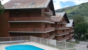 Ein mehrstöckiges Gebäude mit Balkonen, einem Schwimmbad und einer Bergkulisse.