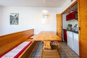 Una mesa de madera con bancos, una cocina con armarios rojos e iluminación de techo fijada a la pared.