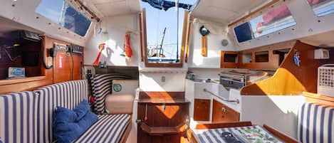A compact boat interior with a seating area, a small kitchen, and a window providing a view of the water.